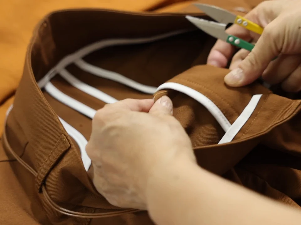 Manos revisando y rematando las costuras de una prenda marrón