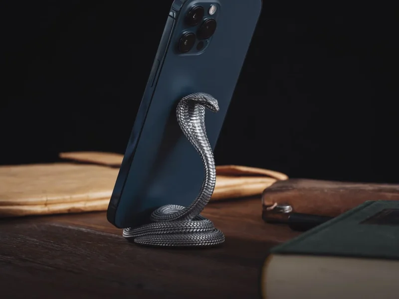 Móvil con funda oscura apoyado mediante un accesorio trasero sobre una mesa