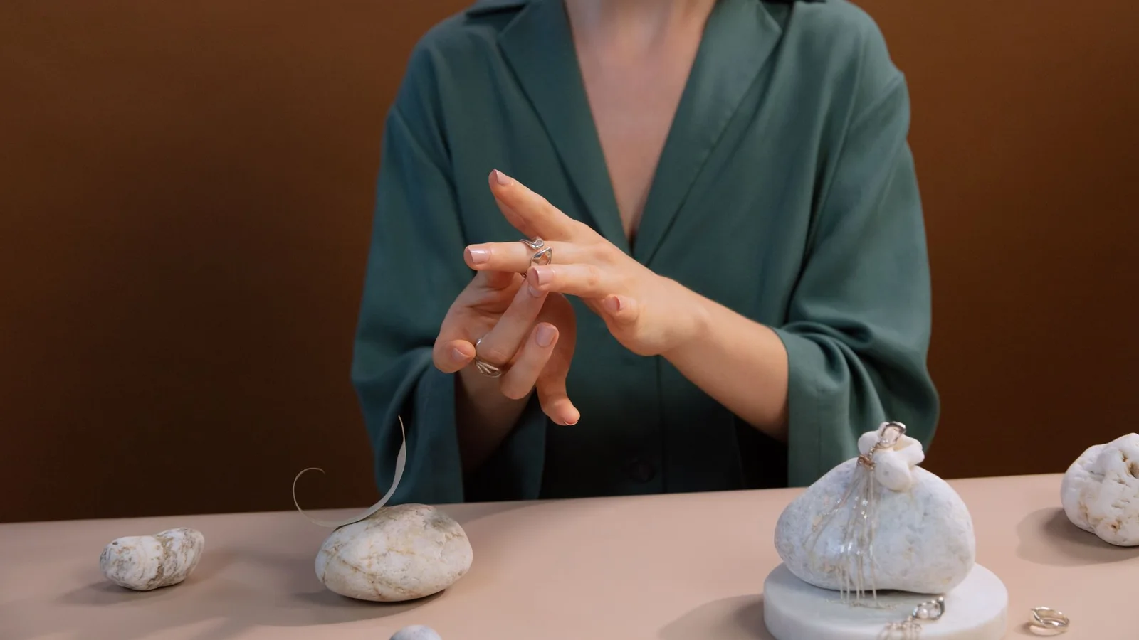 Mujer con blusa verde probándose un anillo en una mesa con joyas.