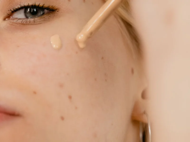 Primer plano de un rostro con pequeñas gotas de maquillaje junto a un aplicador.
