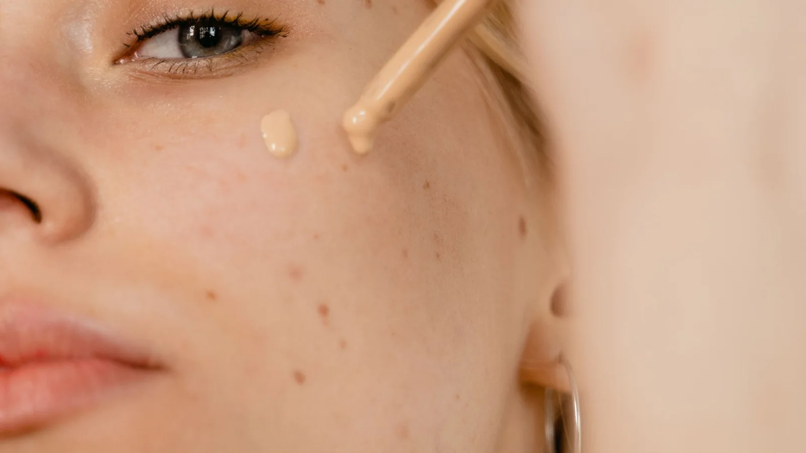 Primer plano de un rostro con pequeñas gotas de maquillaje junto a un aplicador.