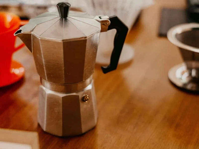 Cafetera sobre una mesa de madera junto a varias tazas