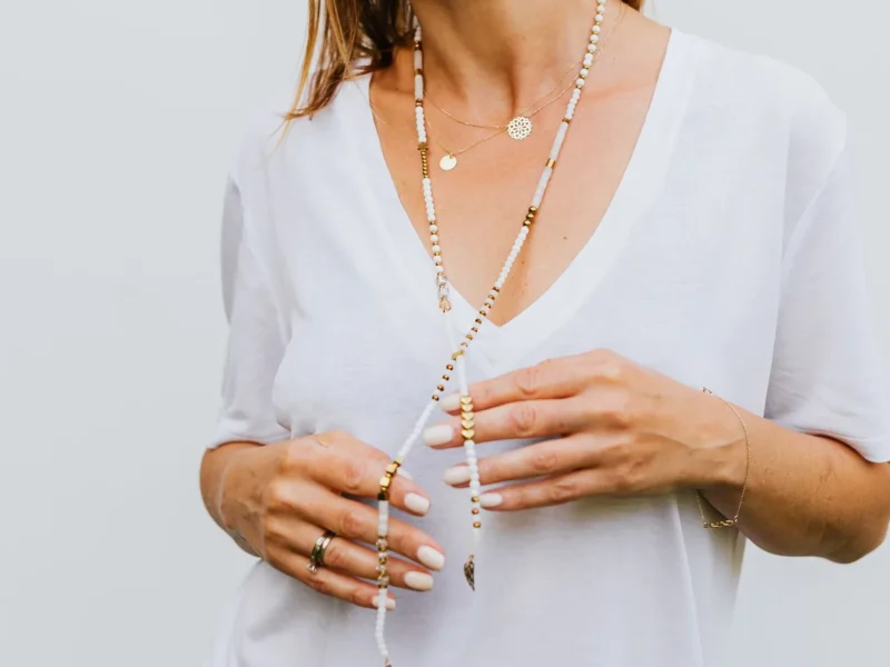 Collares superpuestos, incluido uno largo de cuentas claras, sobre una blusa blanca con escote en V.