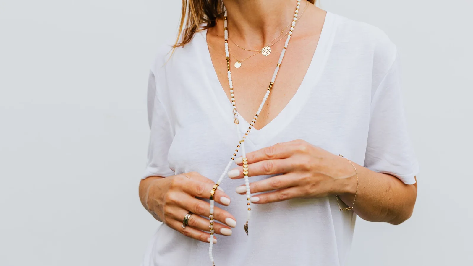 Collares superpuestos, incluido uno largo de cuentas claras, sobre una blusa blanca con escote en V.