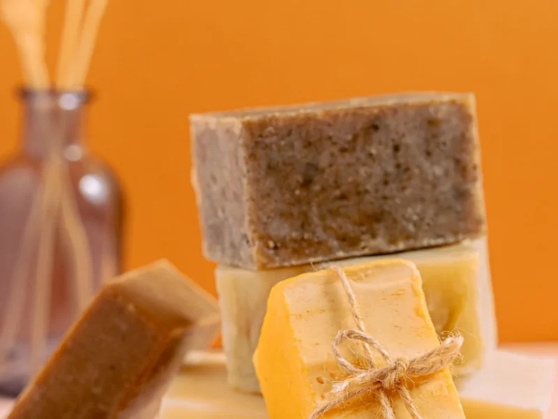 Pastillas de jabón apiladas en distintos tonos y texturas sobre un fondo naranja.