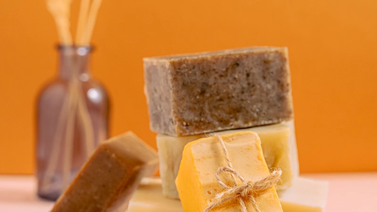 Pastillas de jabón apiladas en distintos tonos y texturas sobre un fondo naranja.