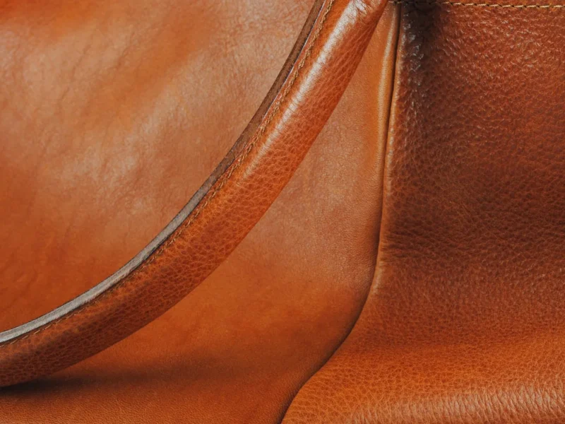 Detalle de un bolso marrón con asa y superficie de piel visible.