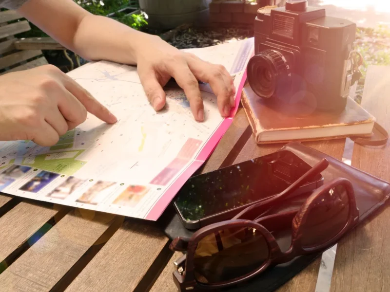 Manos señalando un mapa en una mesa junto a una cámara