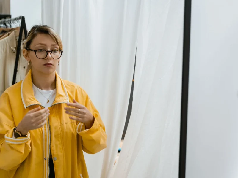 Mujer observando en un espejo su conjunto con chaqueta amarilla