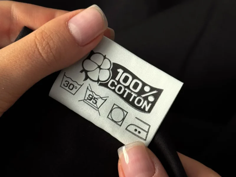 Manos sosteniendo una etiqueta textil con composición y símbolos de cuidado