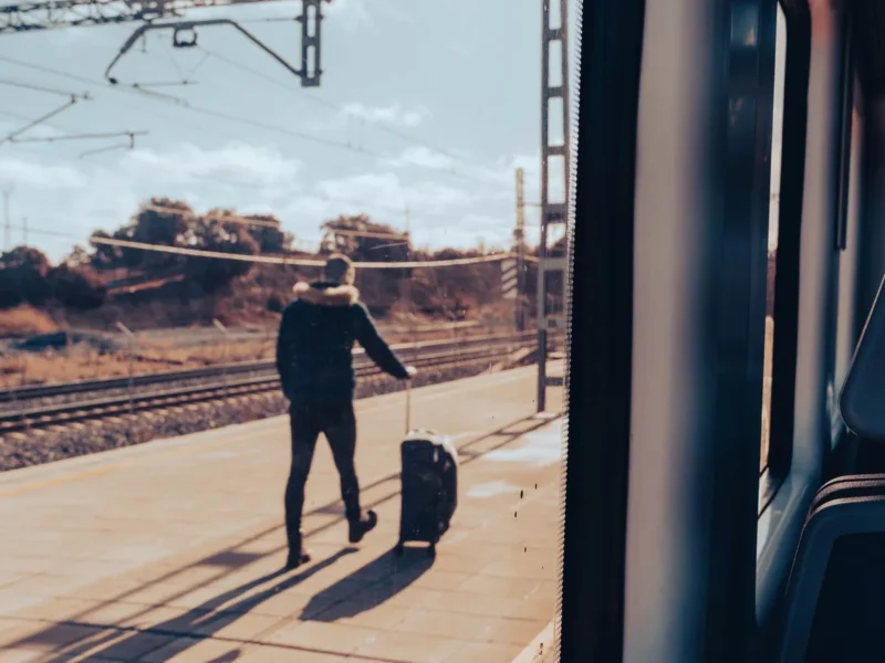 Viajero con maleta en un andén visto desde el interior de un tren