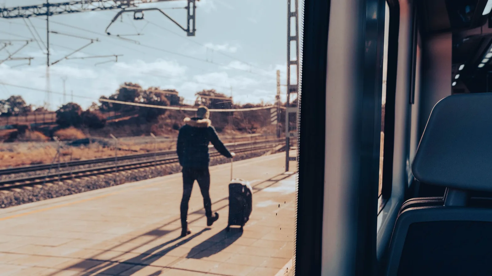 Viajero con maleta en un andén visto desde el interior de un tren