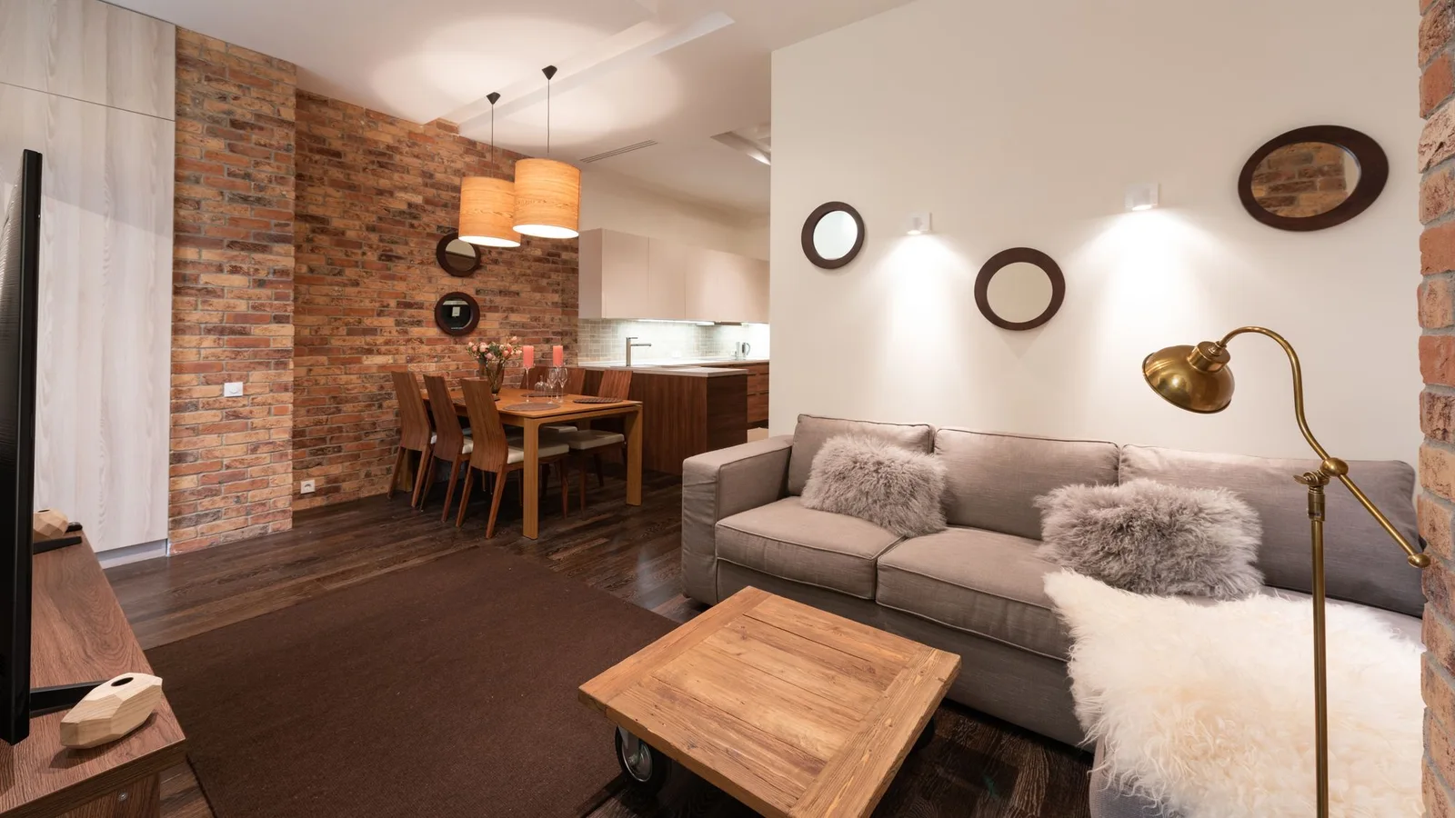 Salón con sofá, lámpara de pie y luminarias sobre la zona de comedor