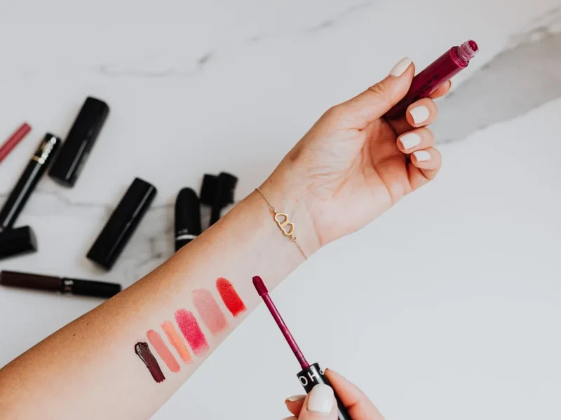 Muestras de diferentes colores de labios en un antebrazo junto a varias barras de maquillaje.