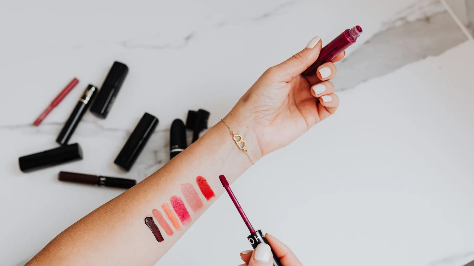 Muestras de diferentes colores de labios en un antebrazo junto a varias barras de maquillaje.