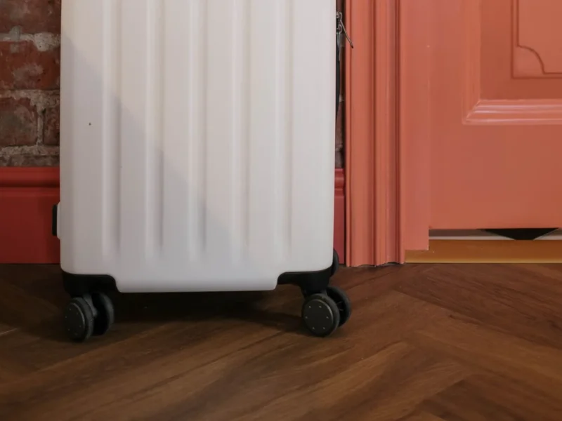 Cuerpo y ruedas de una maleta clara junto a una puerta rosa