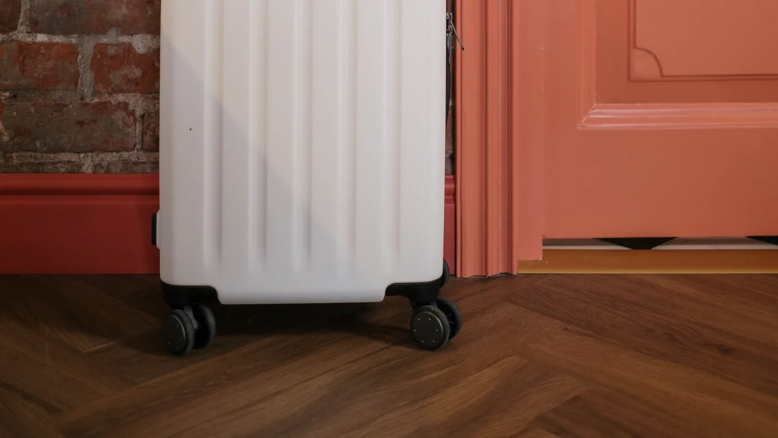 Cuerpo y ruedas de una maleta clara junto a una puerta rosa