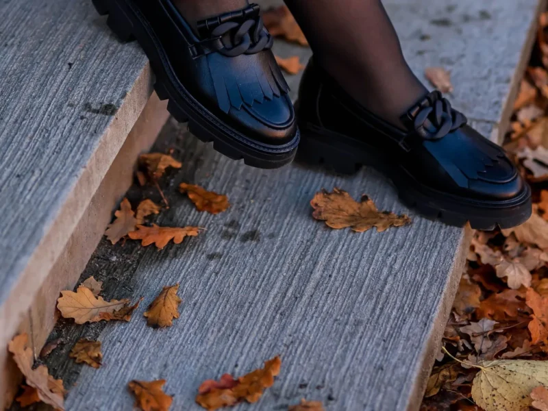 Mocasines negros con detalle metálico junto a unas hojas caídas