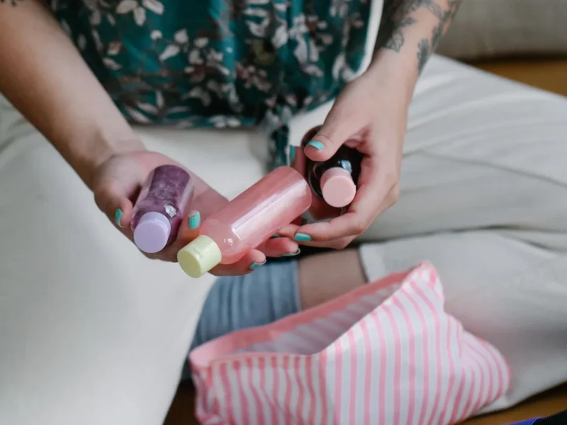 Manos seleccionando tres envases pequeños junto a un neceser de rayas rosas abierto