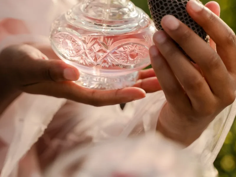 Manos sosteniendo un frasco de perfume de cristal con pulverizador de pera.