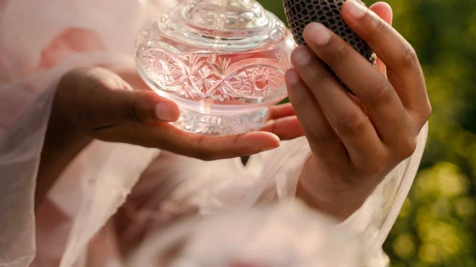 Manos sosteniendo un frasco de perfume de cristal con pulverizador de pera.