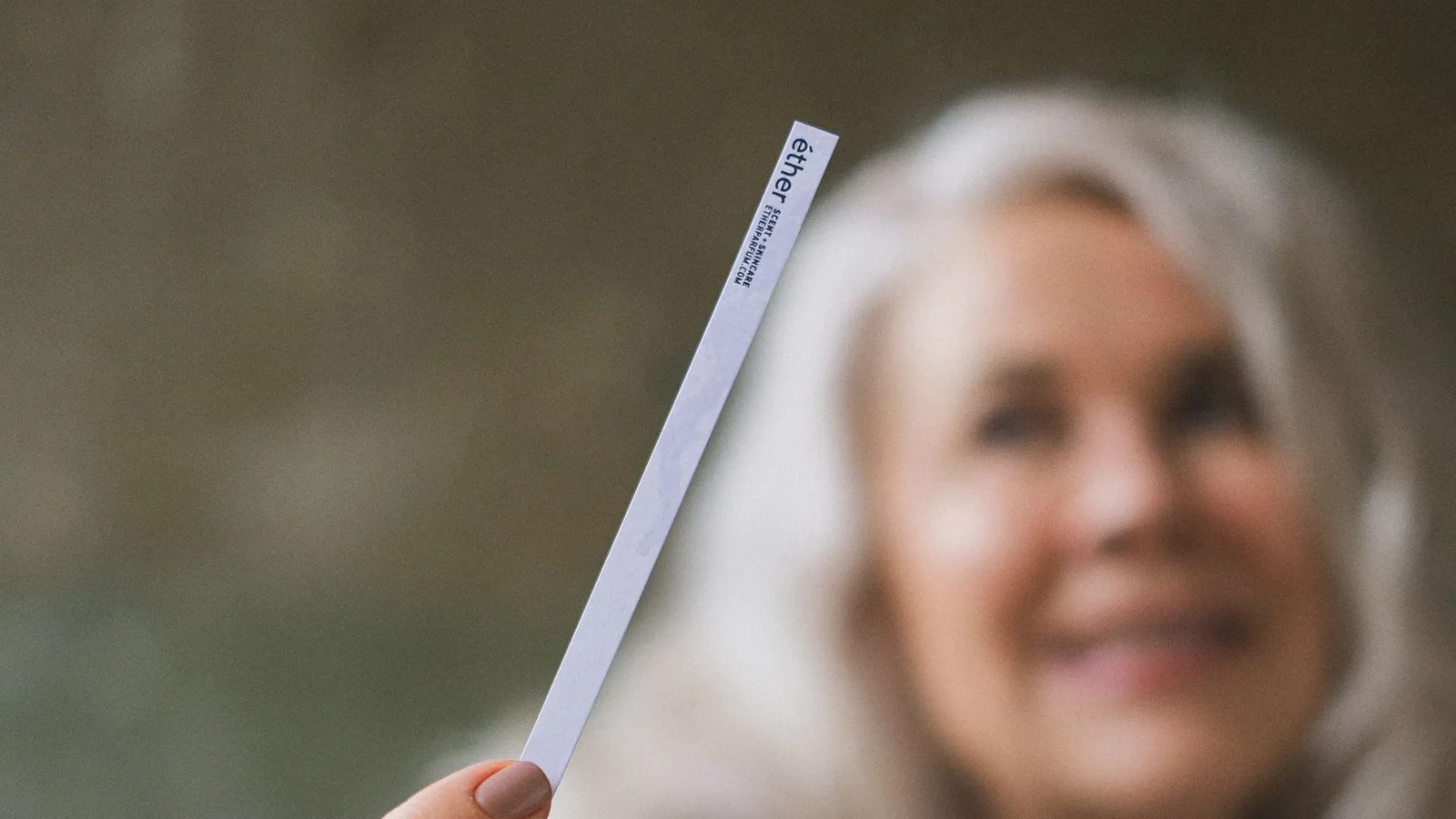Mujer sosteniendo una tira de papel cerca del rostro para percibir una fragancia.
