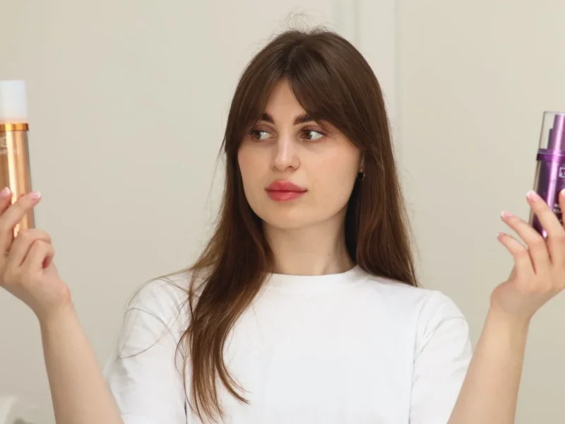 Mujer mirando dos productos cosméticos que sostiene por separado en las manos.