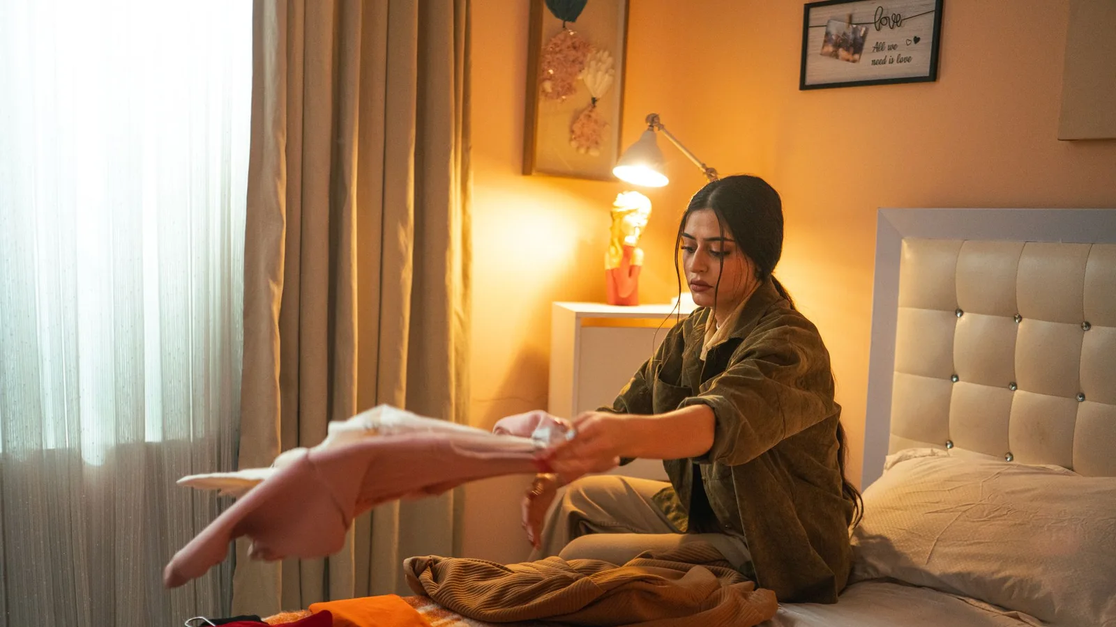 Mujer organizando prendas sobre una cama en una habitación luminosa