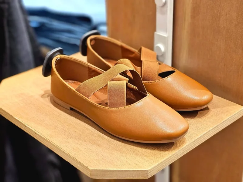Zapatos planos de color cuero con tira cruzada sobre una balda de madera
