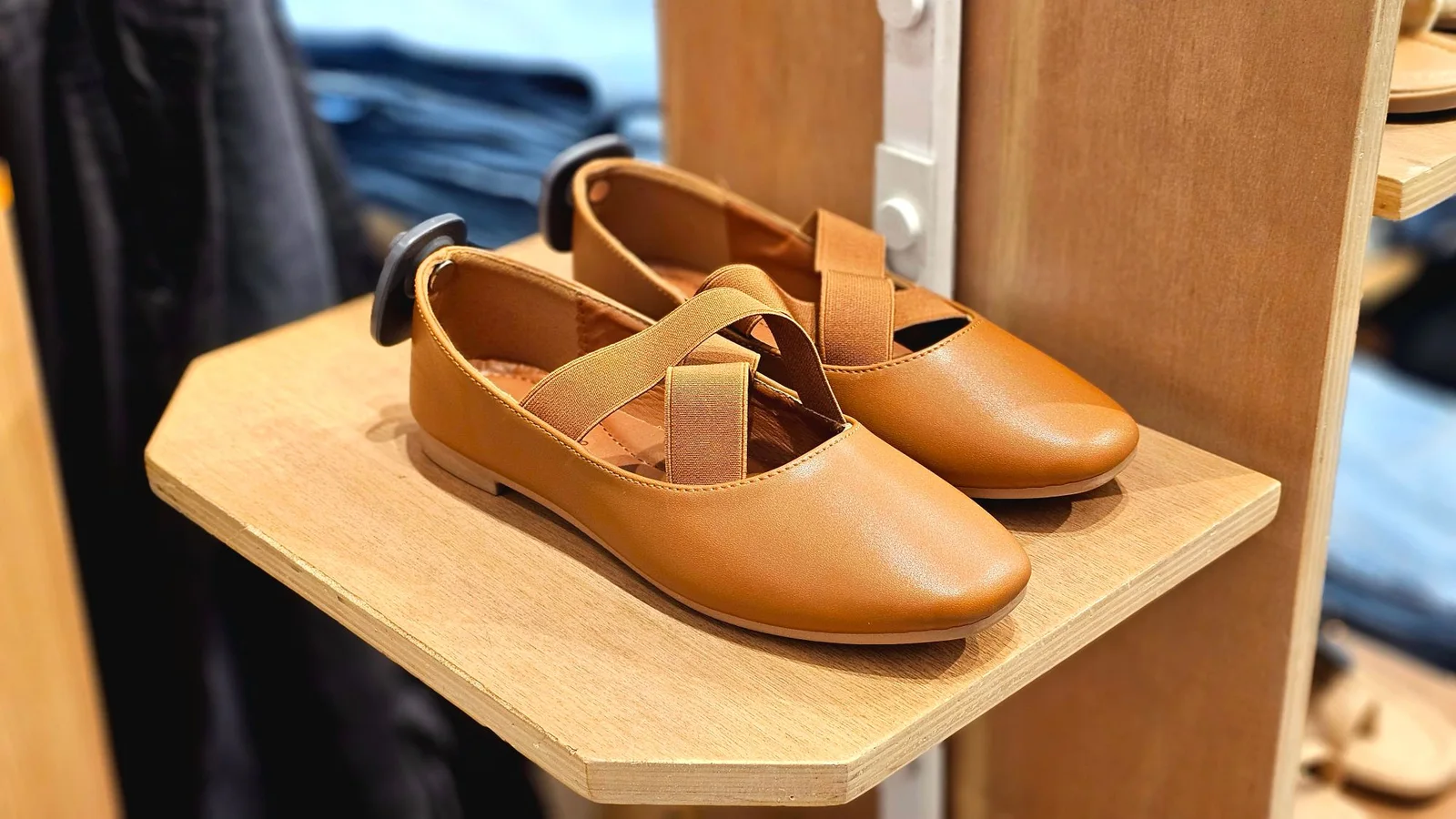 Zapatos planos de color cuero con tira cruzada sobre una balda de madera